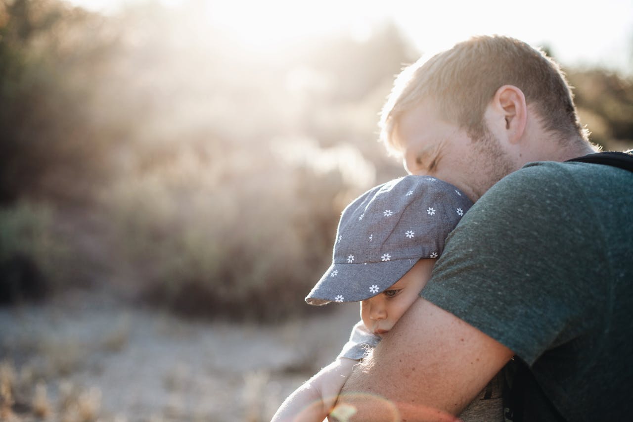 A father lovingly embraces his baby outdoors on a sunny day. Perfect for Father's Day themes.