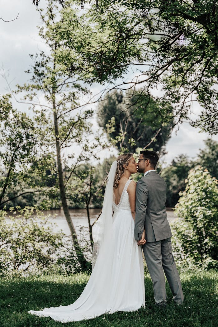 Bride and groom share a kiss by a scenic riverside during their wedding day.
